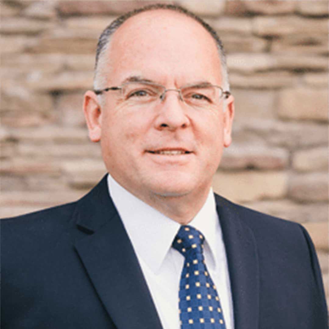Portrait of Jay Varney in a navy suit and blue patterned tie